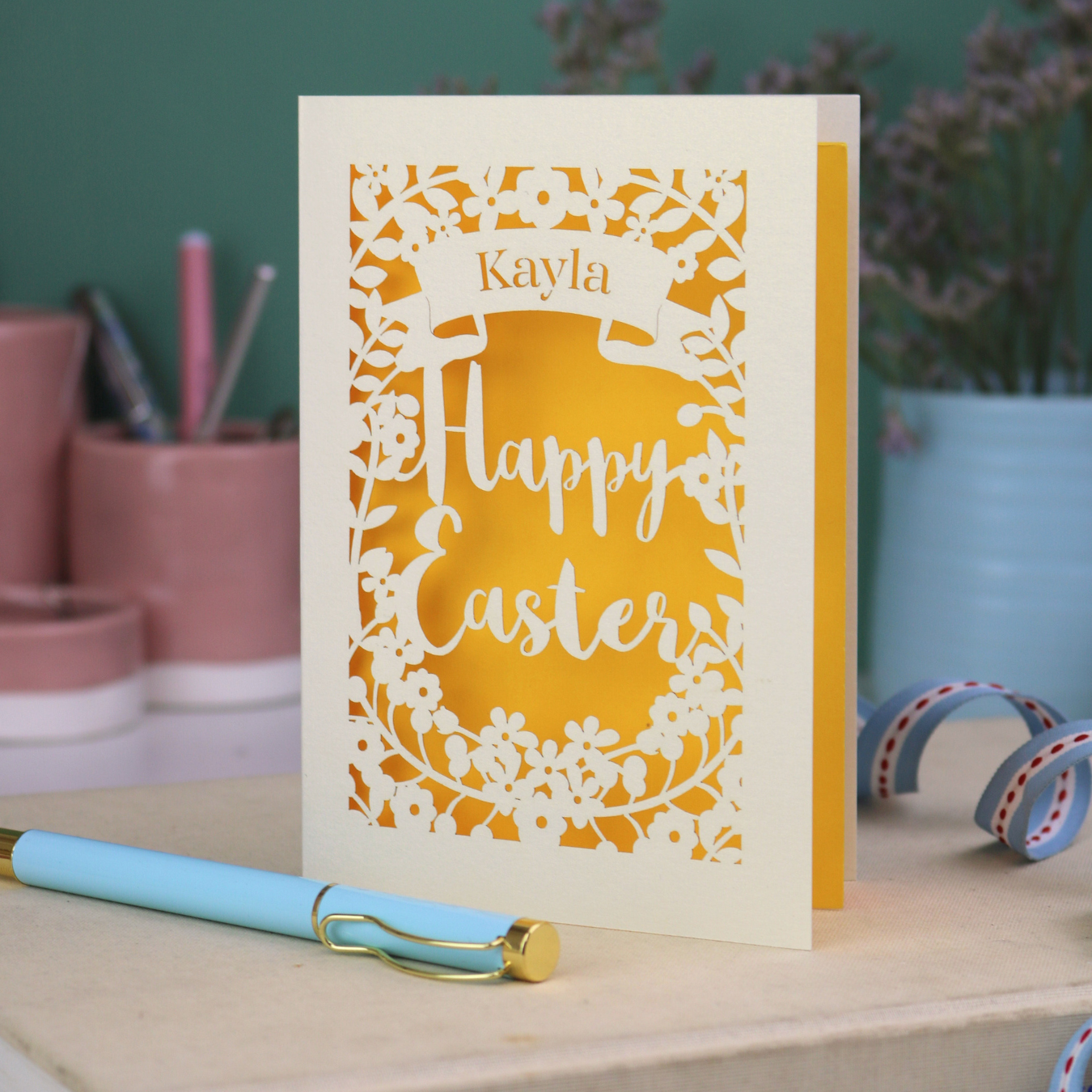 Personalised laser cut Easter card with 'Happy Easter' and 'Kayla' text on a desk with stationery items.