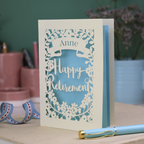 Greeting card with 'Happy Retirement' text on a wooden surface with decorative items.