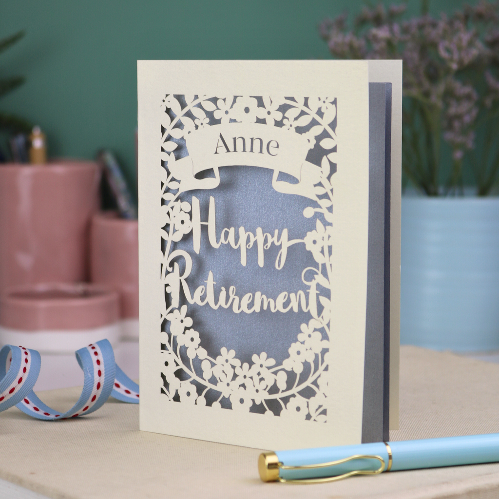 Laser-cut 'Happy Retirement' card with personalized name on a decorative surface.
