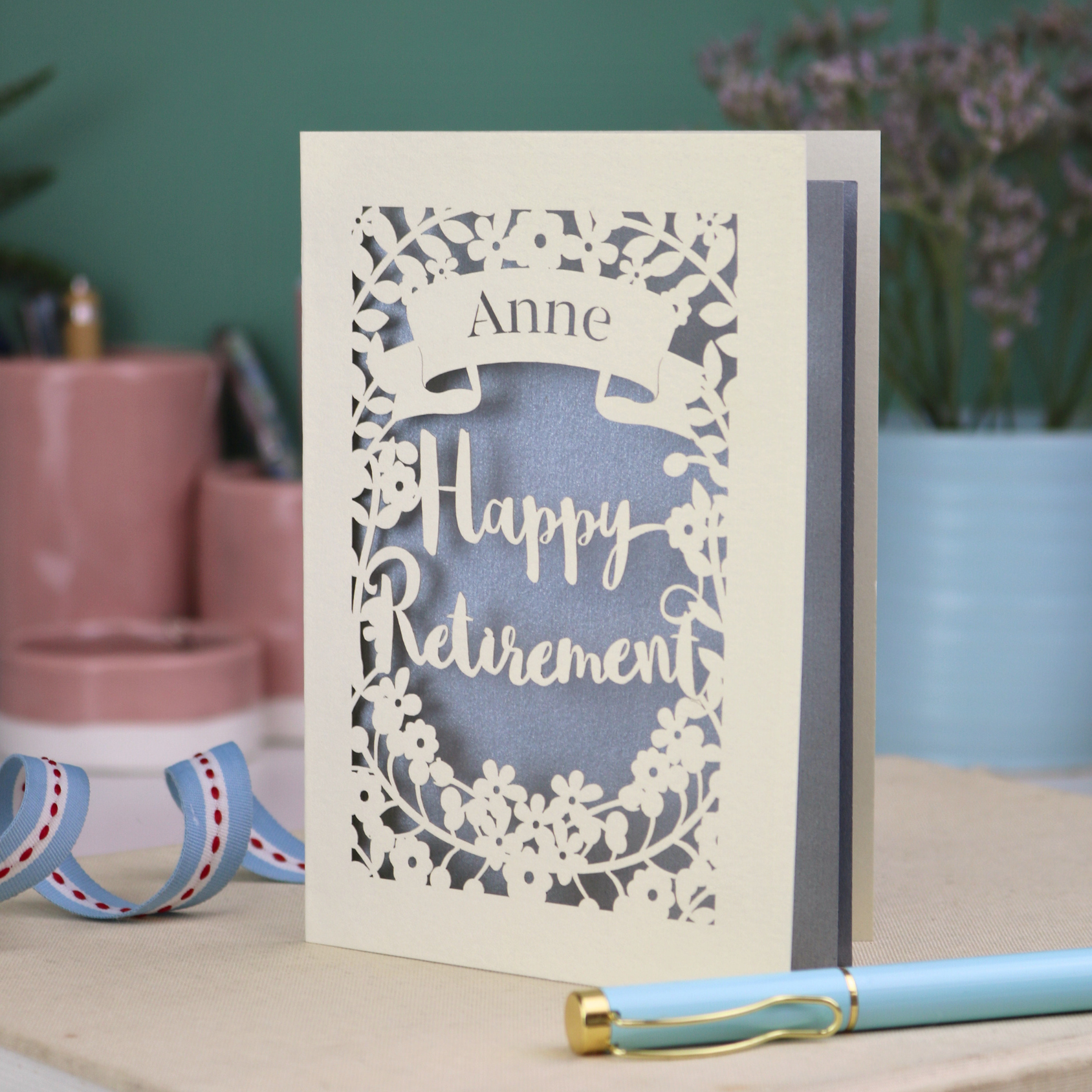 Laser-cut 'Happy Retirement' card with personalized name on a decorative surface.