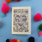 Laser cut Valentines Card with 'Josh you make me happy' text on a blue background with colourful pom-poms