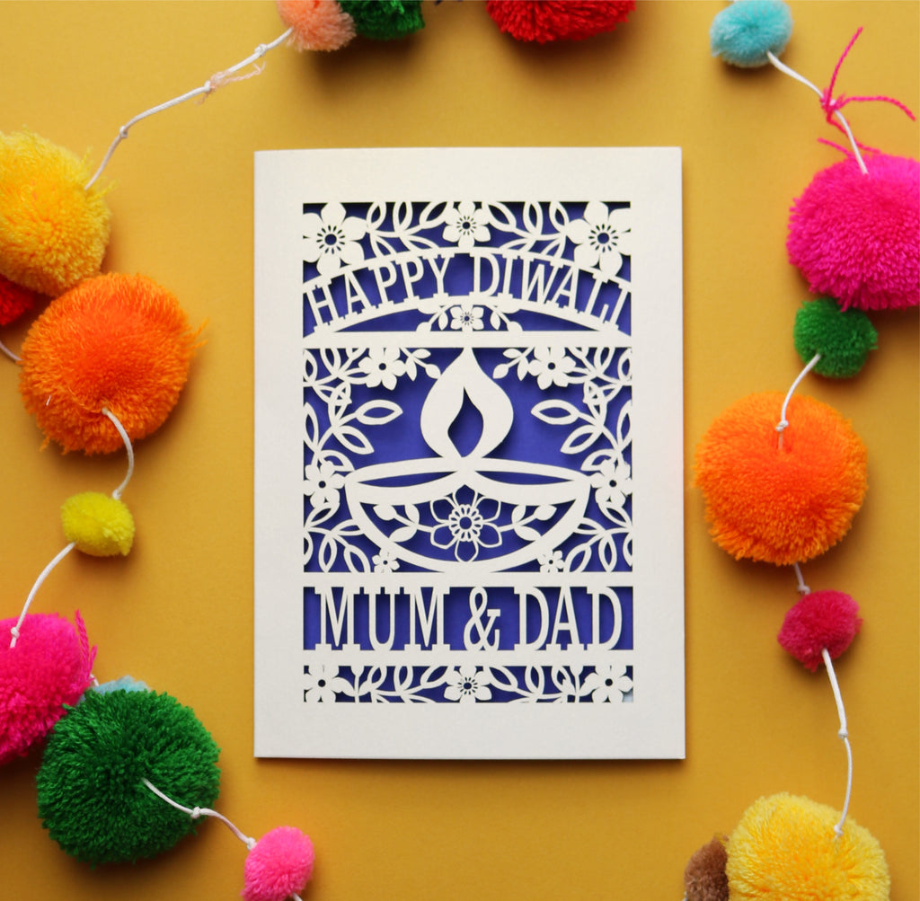 Decorative Diwali card with 'Happy Diwali' and 'Mom & Dad' text on a yellow background with colourful pom-poms.