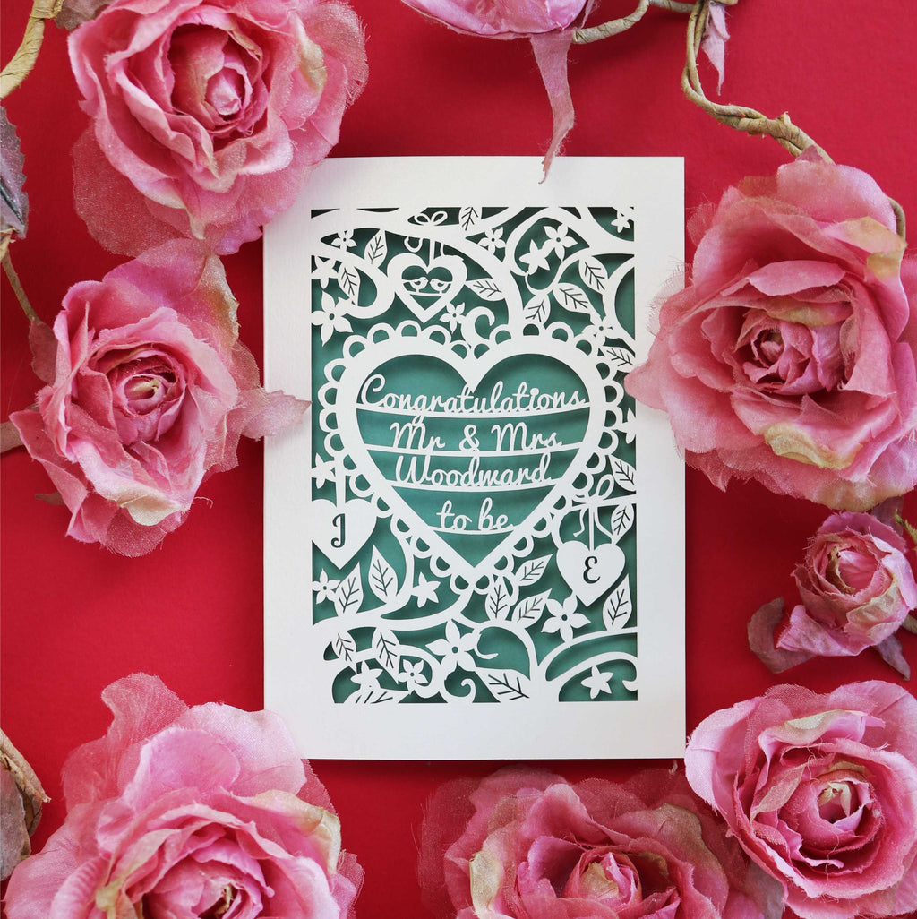 A personalised engagement card, laser cut with floral details and a heart in the centre. Heart contains the words "Congratulations Mr and Mrs Woodward to be"