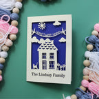 A cut out home sweet home card for a housewarming. Card has a laser cut banner with the words "Home sweet home" and at the bottom of the card is cut out personalised text with the recipient's name. In the centre of the card is a laser cut house design with a cat and flowers