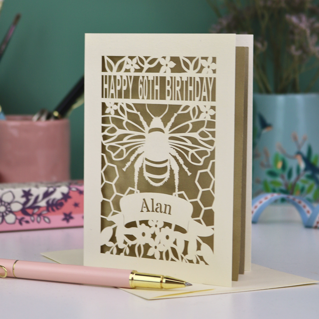 Laser-cut husband birthday card with cut out bee design and 'Happy 60th Birthday Alan' text on a gold background.