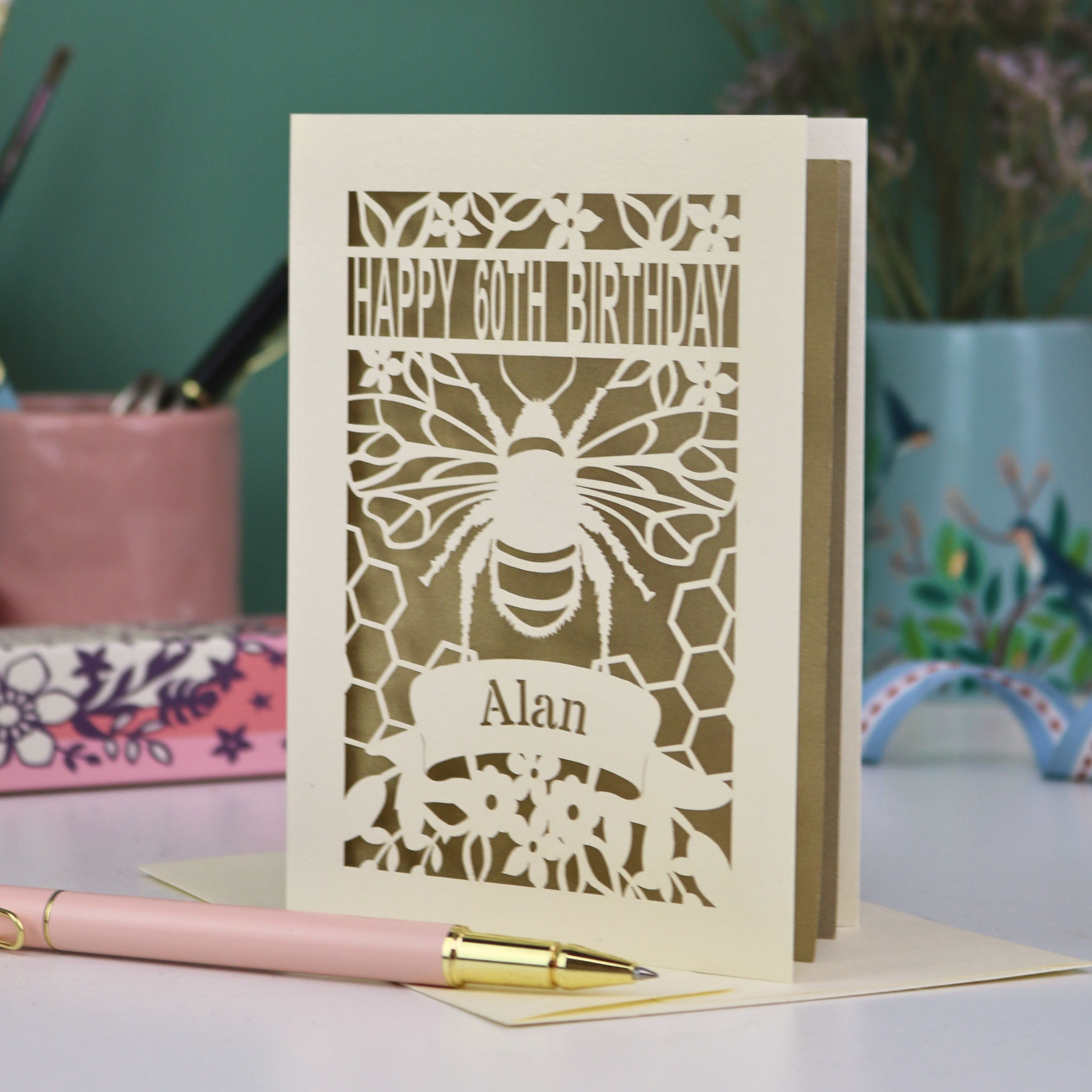 Laser-cut husband birthday card with cut out bee design and 'Happy 60th Birthday Alan' text on a gold background.