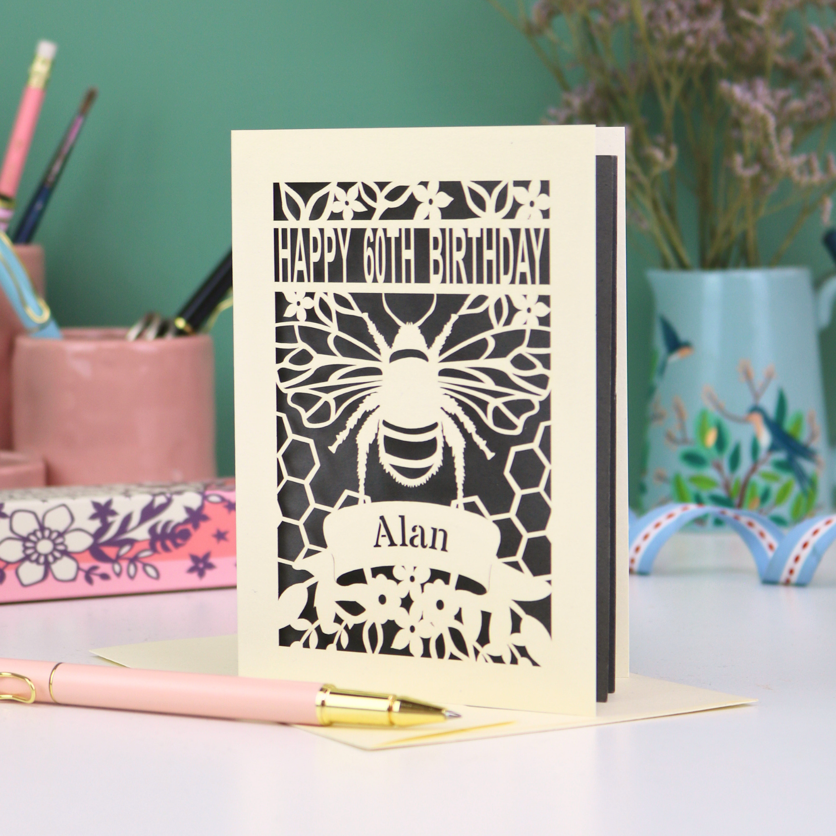 Laser-cut husband birthday card with cut out bee design and 'Happy 60th Birthday Alan' text on a grey background.