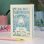 Birthday card with bee design and 'Happy 60th Birthday Alan' text on a desk with stationery items.