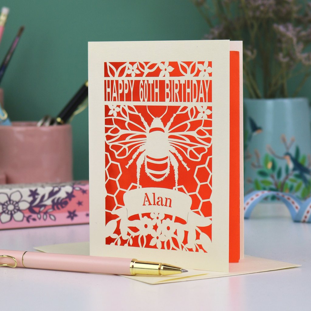 Laser-cut husband birthday card with cut out bee design and 'Happy 60th Birthday Alan' text on an orange background.