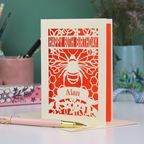 Laser-cut husband birthday card with cut out bee design and 'Happy 60th Birthday Alan' text on an orange background.