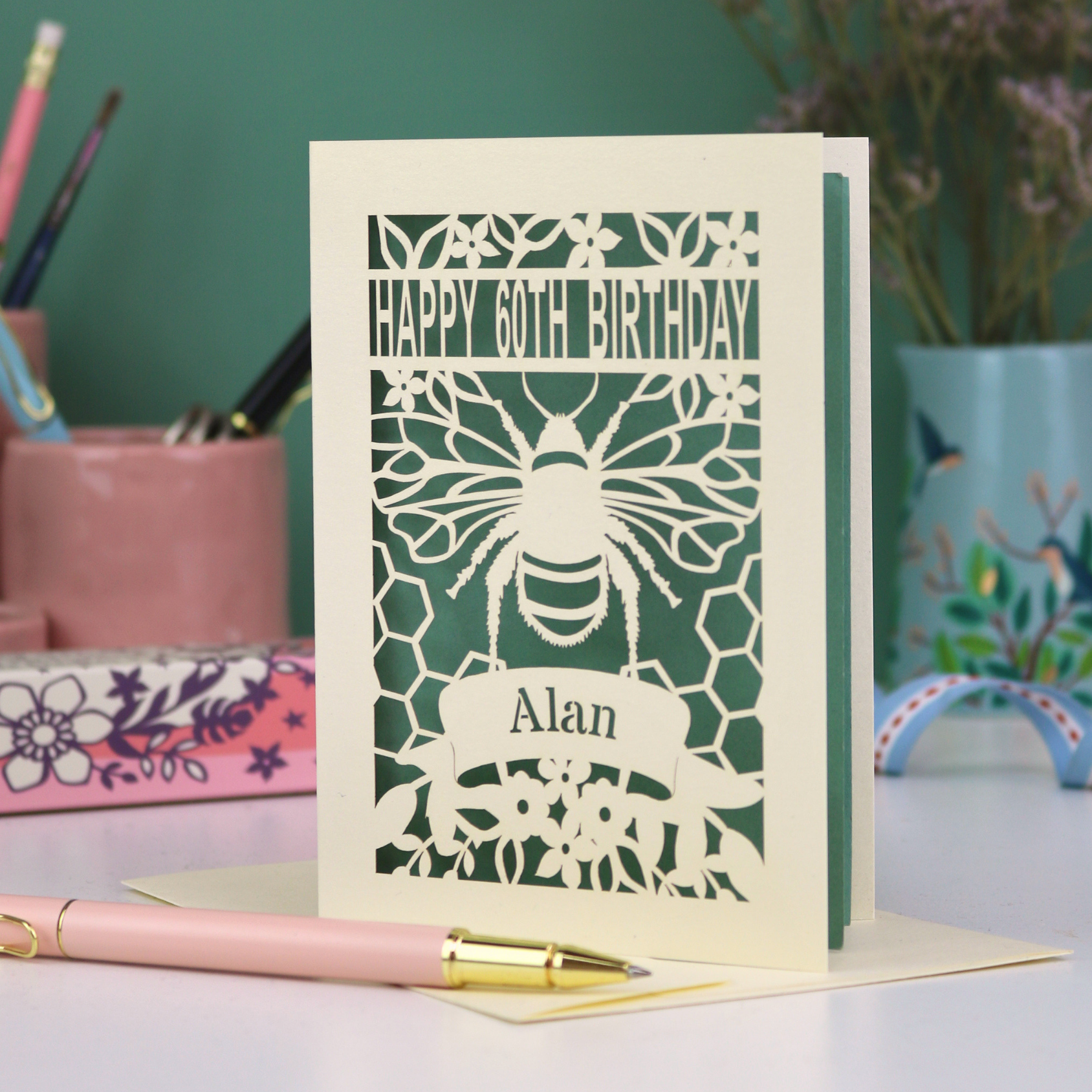 Laser-cut husband birthday card with cut out bee design and 'Happy 60th Birthday Alan' text on a green background.