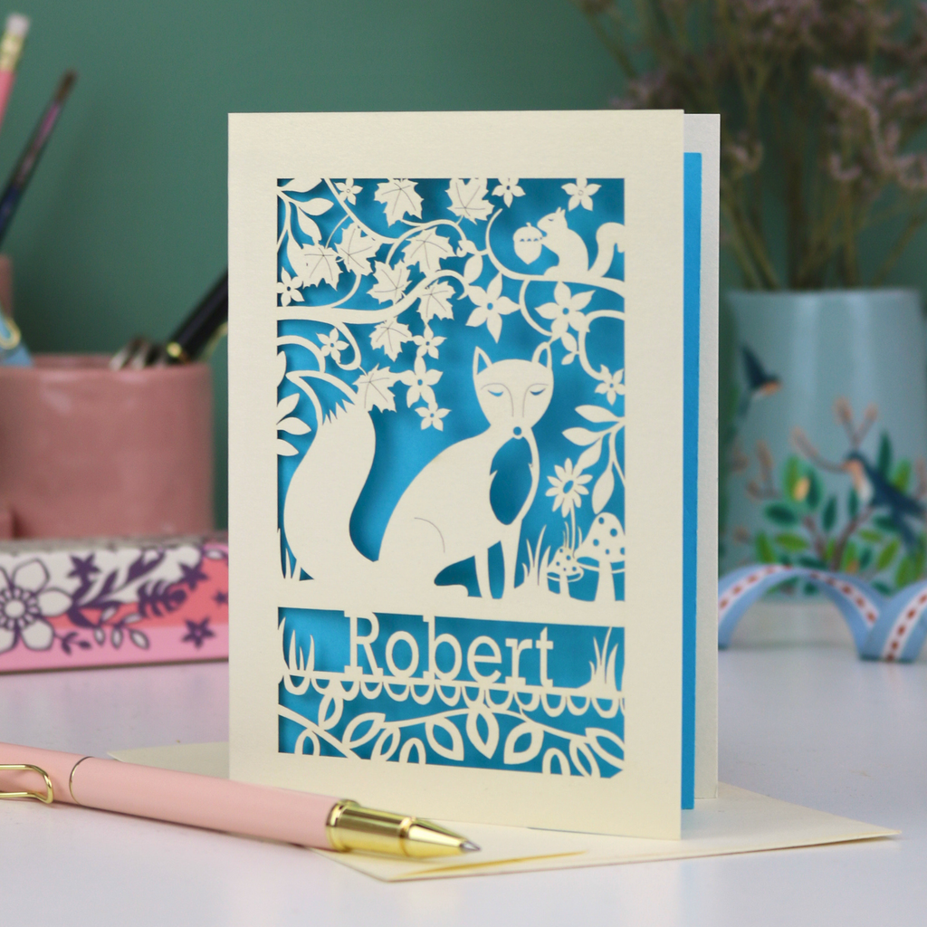 Laser cut birthday Card with fox design and 'Robert' text on a desk with stationery items.
