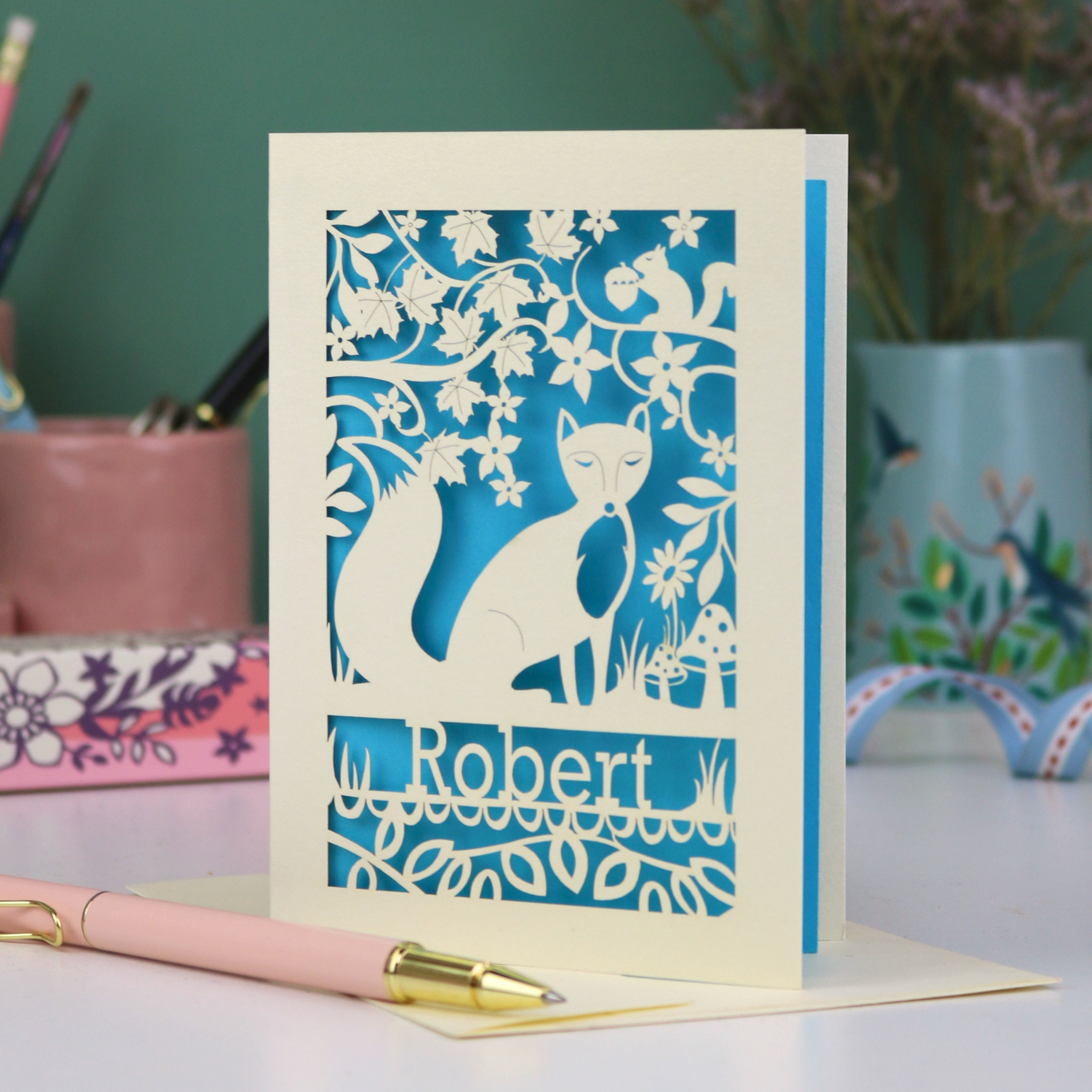 Laser cut birthday Card with fox design and 'Robert' text on a desk with stationery items.