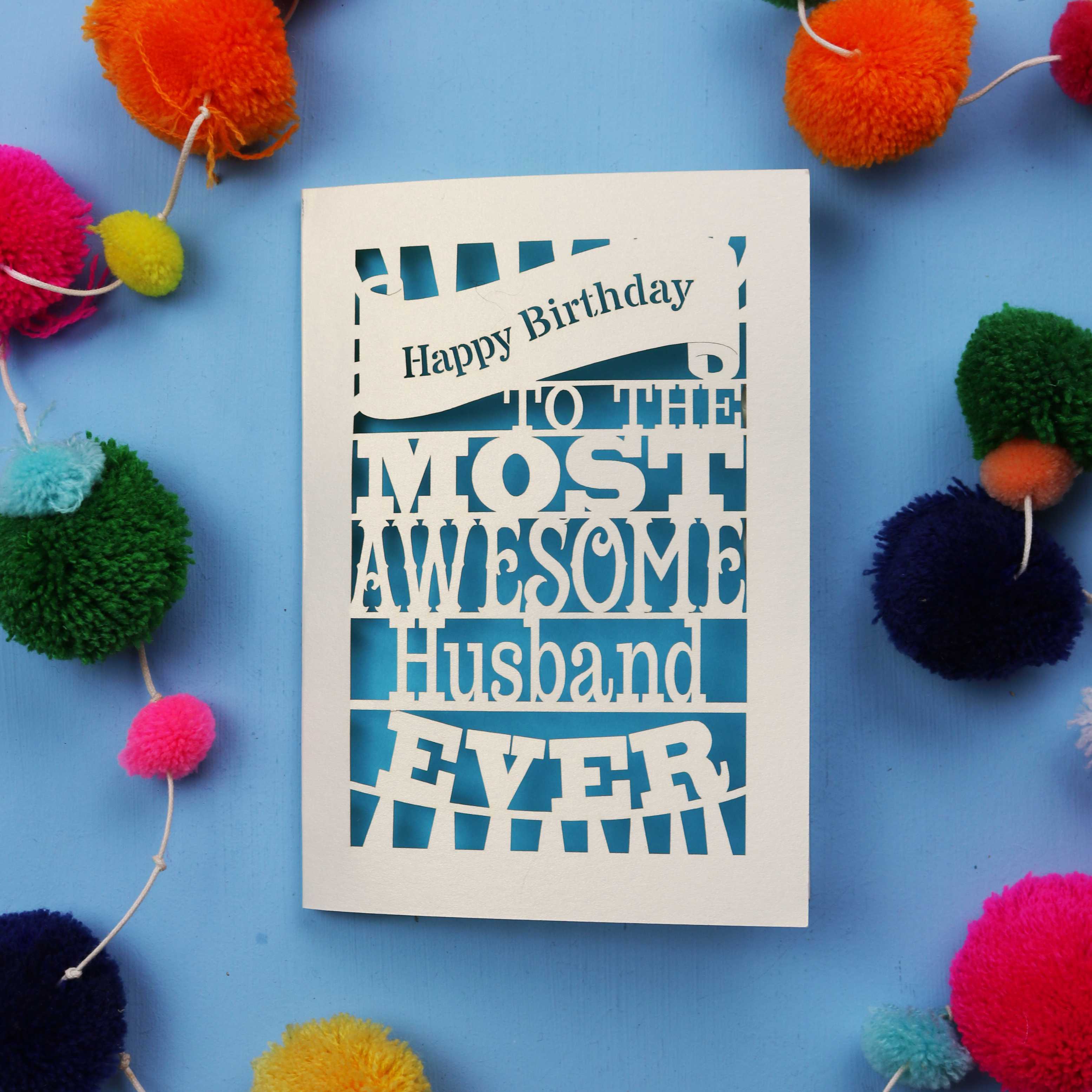 Paper cut Husband Birthday card for the most awesome husband ever on a blue background with colourful pom-poms.