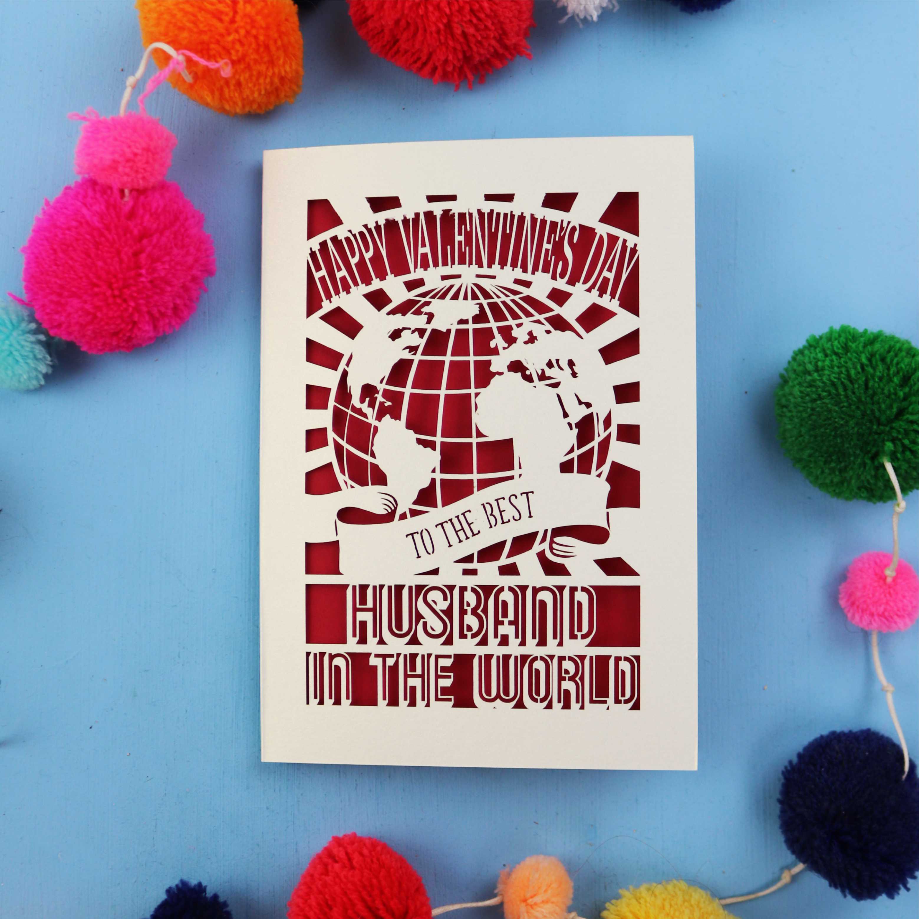 Laser Cut Husband Valentine's Card with 'Happy Valentine's Day' and 'To the best husband in the world' text on a blue background with colourful pom-poms.