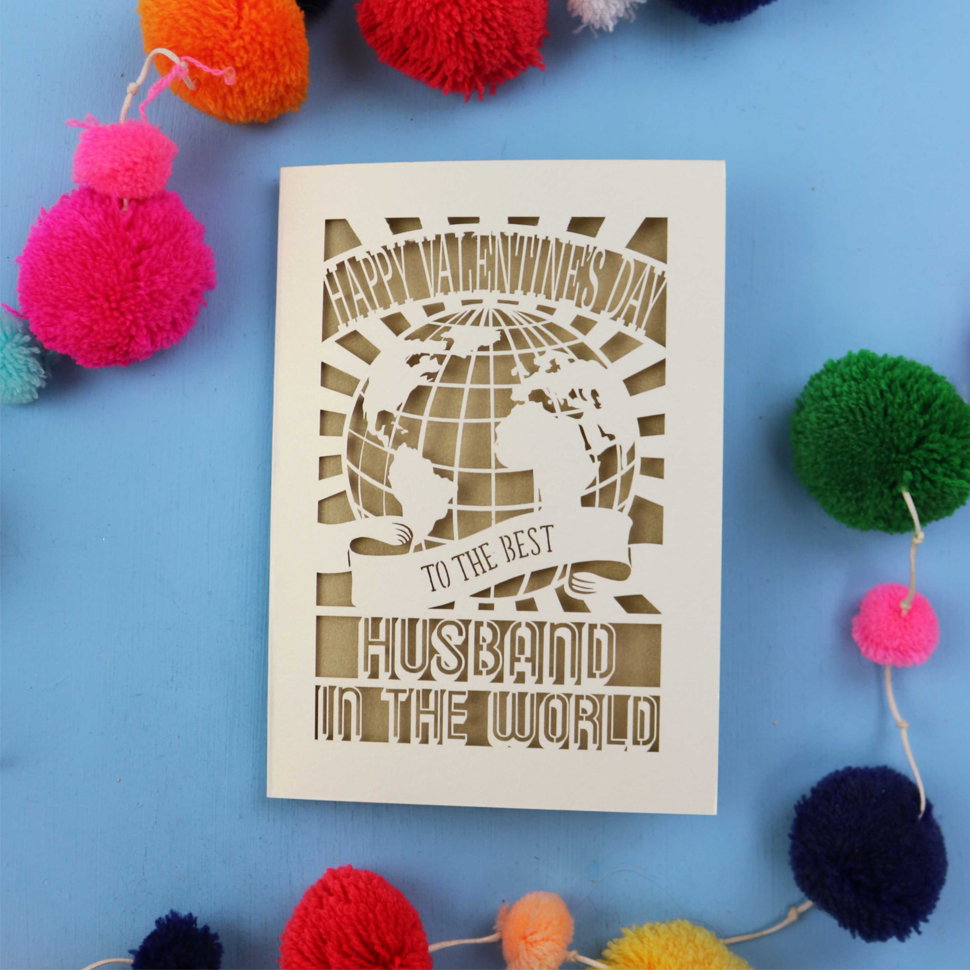 Cut out Husband Valentine's Card with 'Happy Valentine's Day' and 'To the best husband in the world' text on a blue background with colourful pom-poms.
