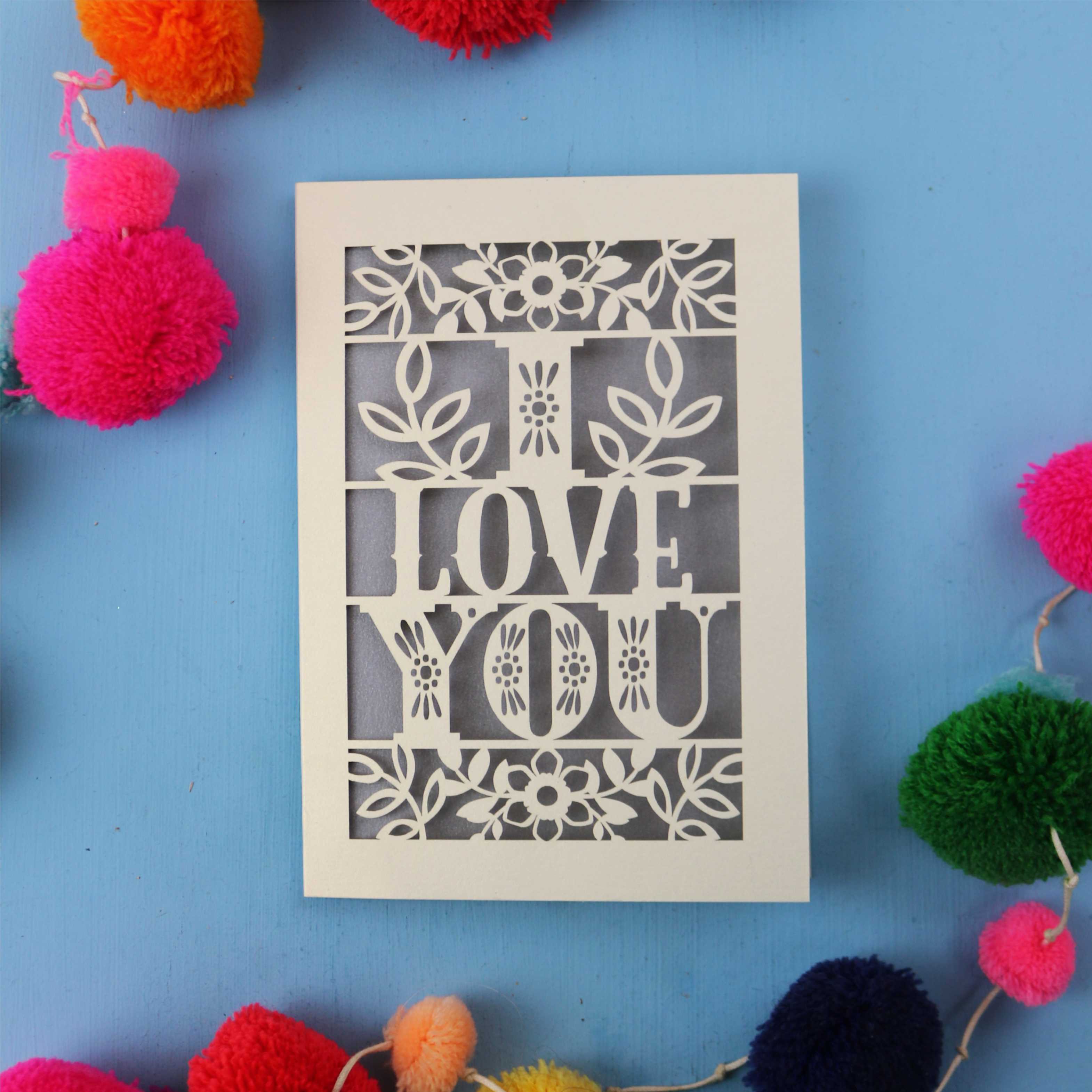 Valentine's Card with 'I LOVE YOU' design surrounded by colourful pom-poms on a blue background