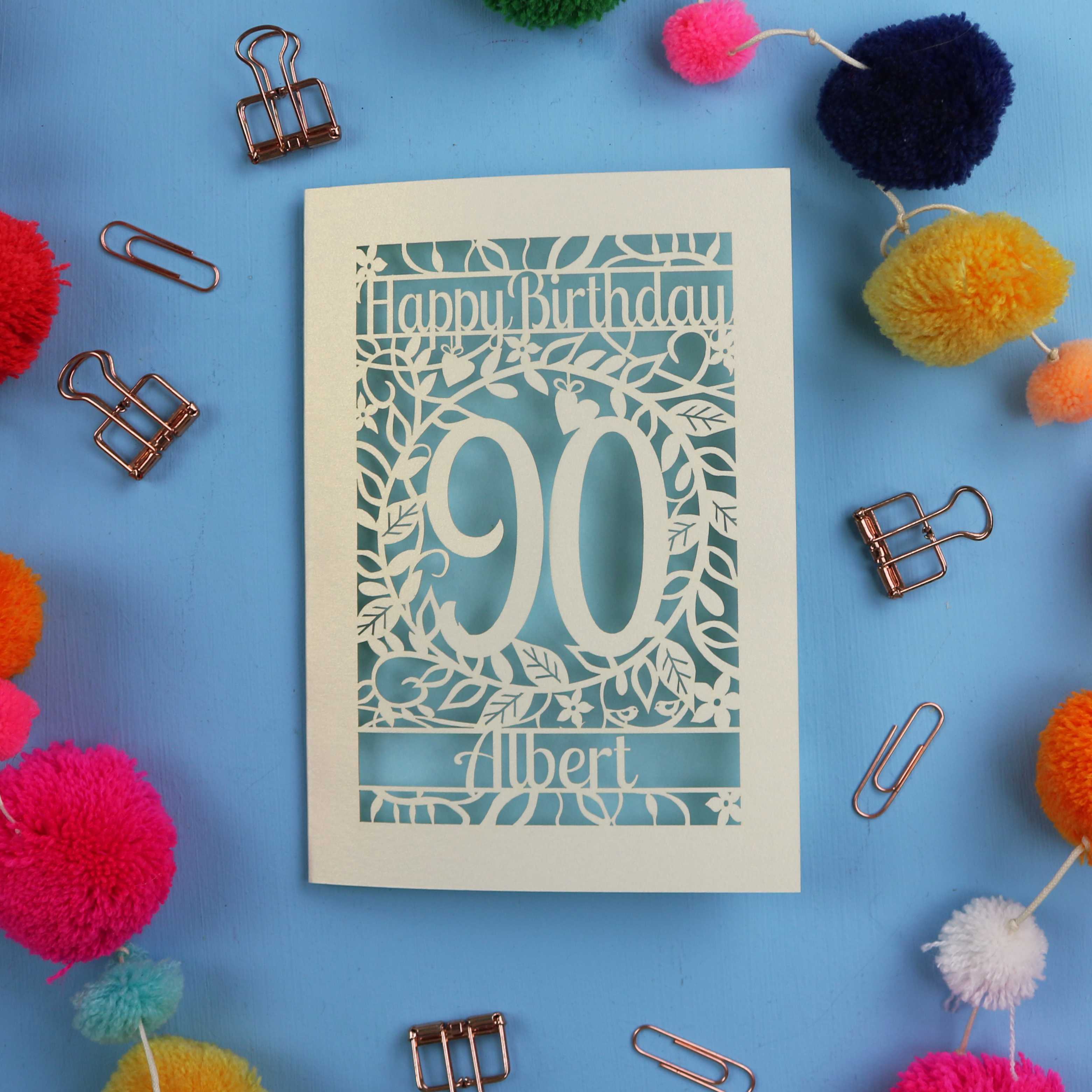 Birthday card with 'Happy Birthday 90 Albert' on a blue background with colourful pom-poms and paper clips.