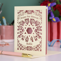 Decorative laser cut card for Bat Mitzvah with floral patterns and a Star of David, on a blurred background.