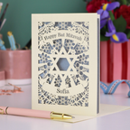 Personalized 'Happy Bat Mitzvah' card with decorative design on a table with stationery items.