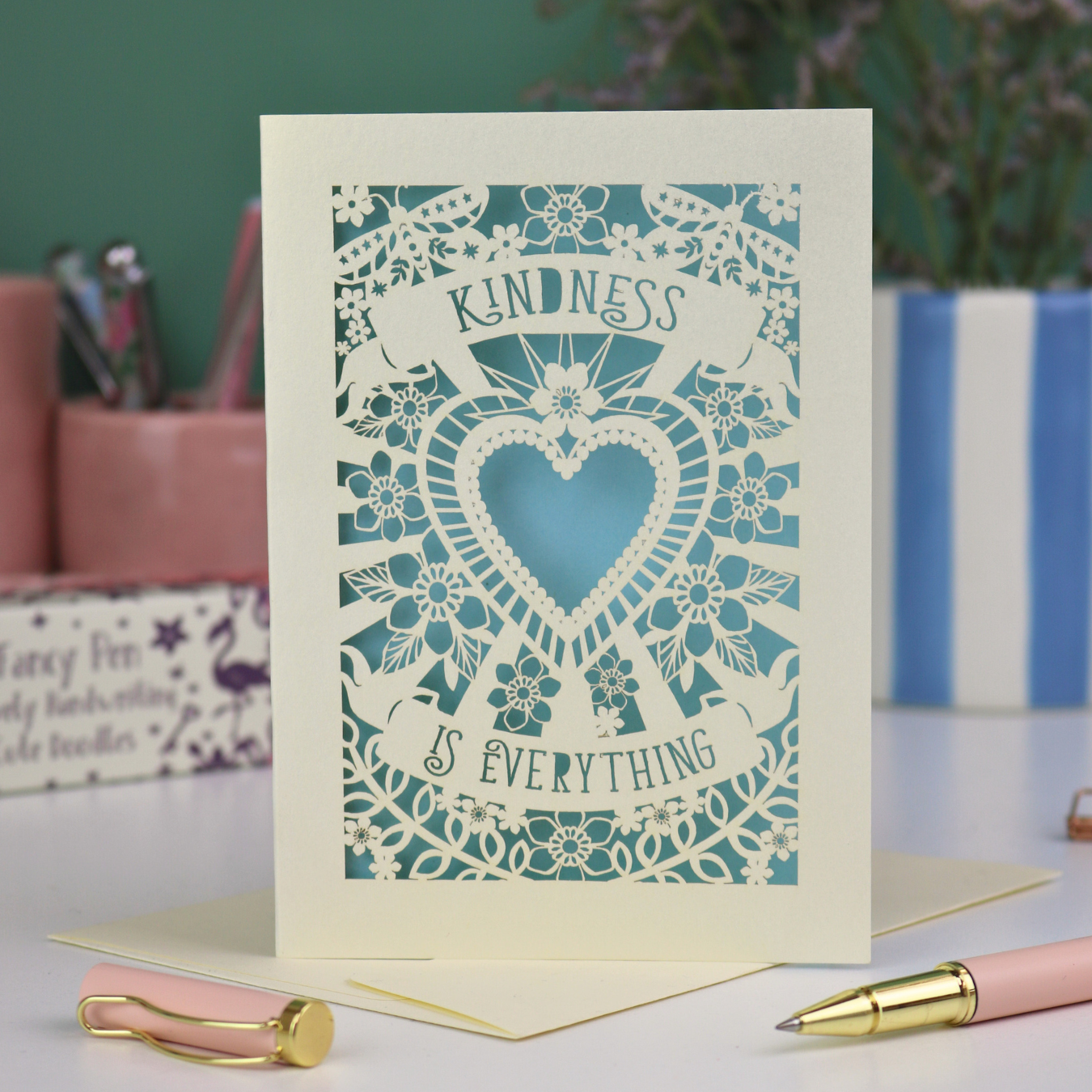 A detailed floral laser cut card with heart shape in the centre and two banners, one above with "Kindness" and one below with "is everything". 