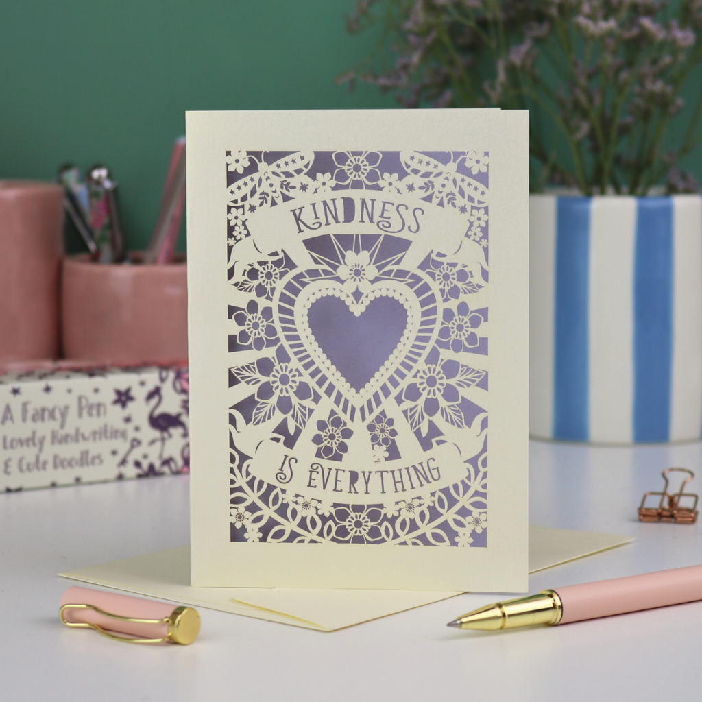 A detailed floral laser cut card with heart shape in the centre and two banners, one above with "Kindness" and one below with "is everything". 