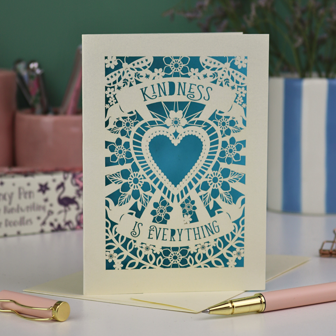 A detailed floral laser cut card with heart shape in the centre and two banners, one above with "Kindness" and one below with "is everything". 