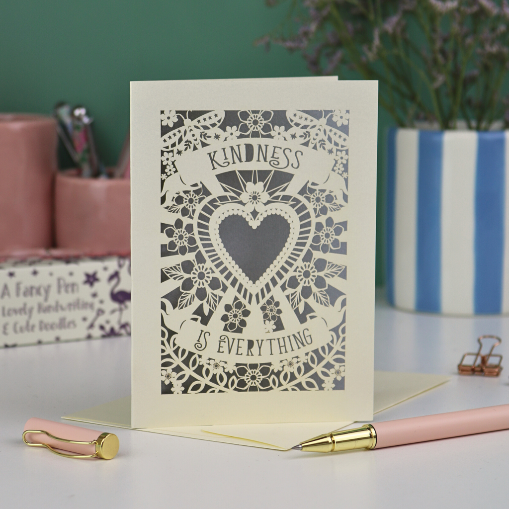 A detailed floral laser cut card with heart shape in the centre and two banners, one above with "Kindness" and one below with "is everything". 
