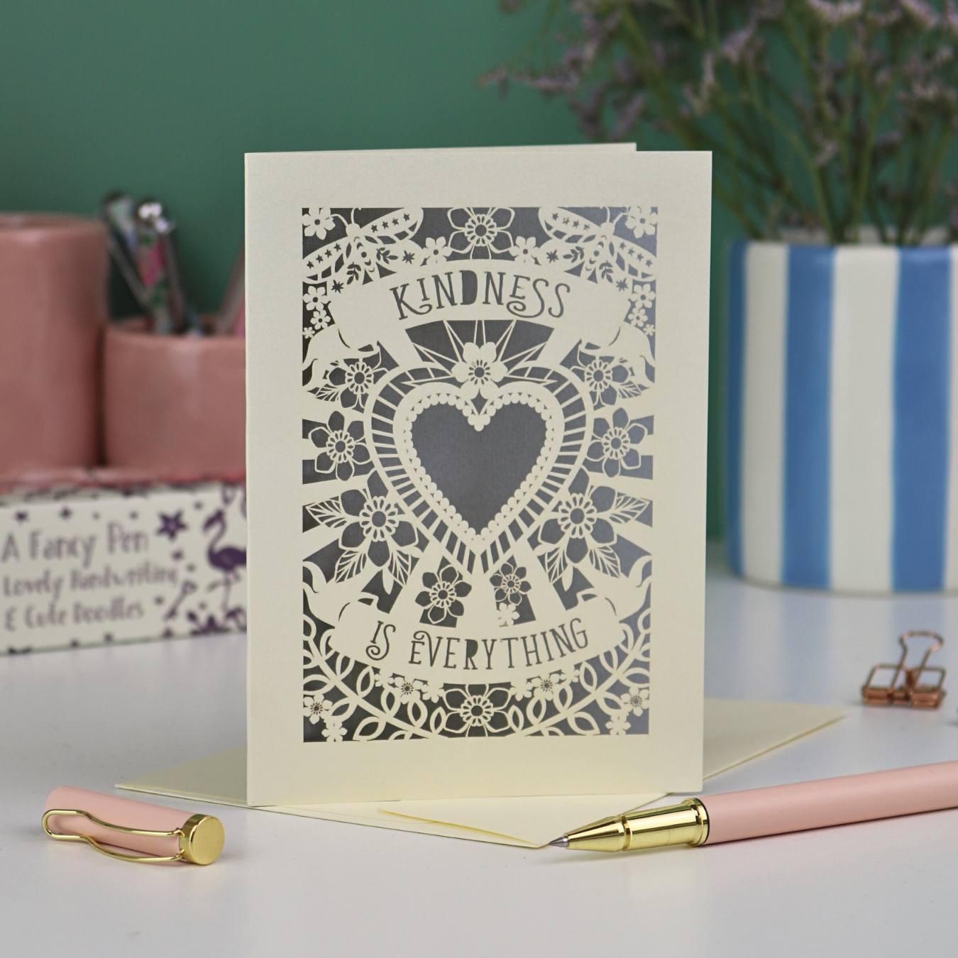 A detailed floral laser cut card with heart shape in the centre and two banners, one above with "Kindness" and one below with "is everything". 