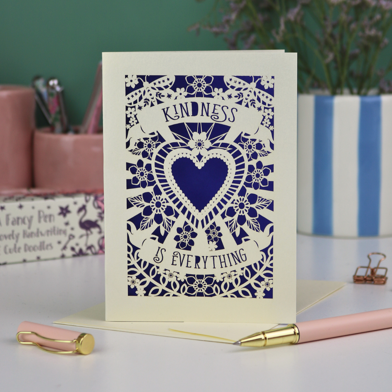 A detailed paper cut card with heart shape in the centre and two banners, one above with "Kindness" and one below with "is everything". 