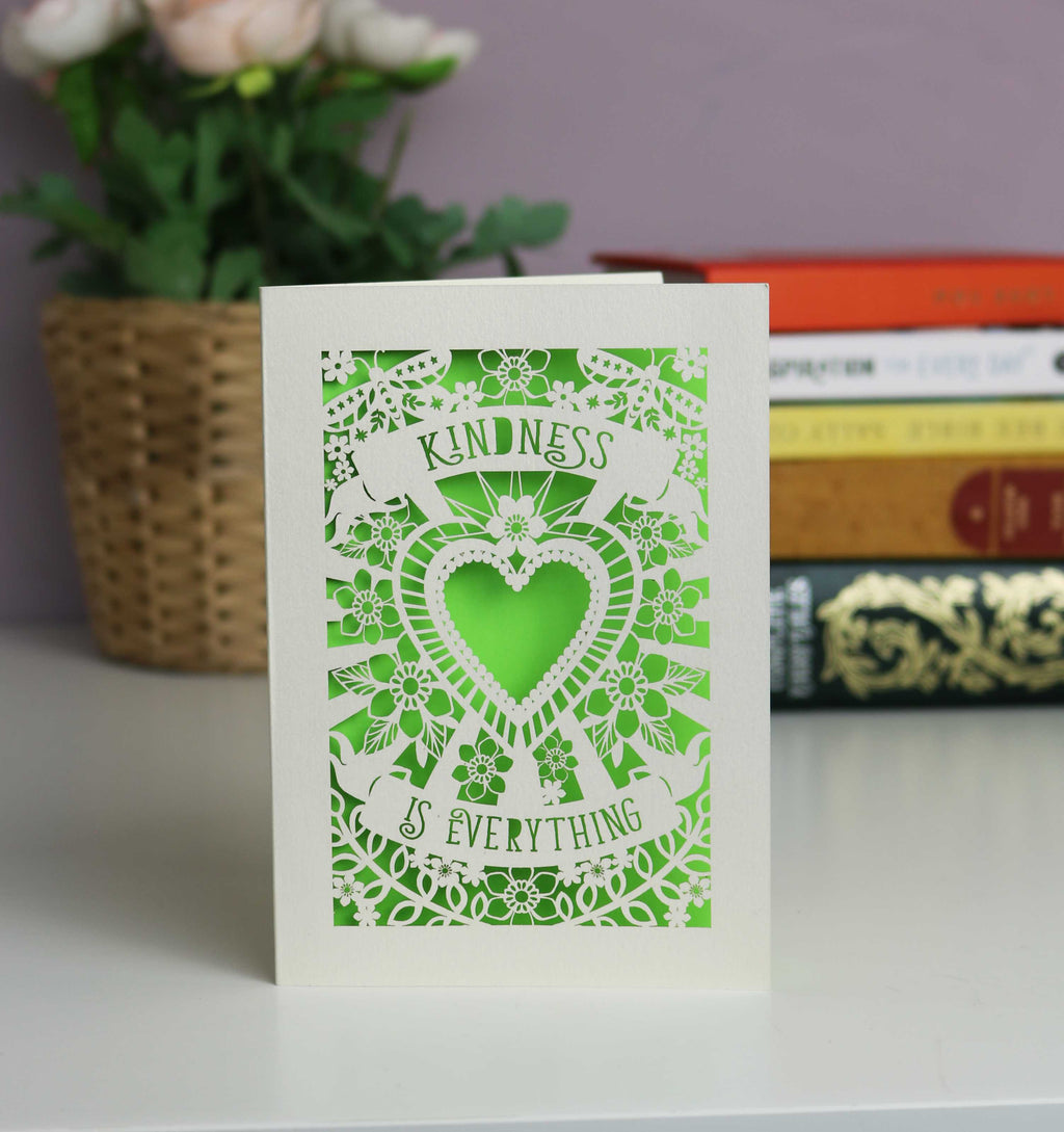 Kindness is everything  lasercut card. Cut from cream card with a bright green insert. Butterflies and lots of flowers around a central heart with the text in two banners above and below the heart.