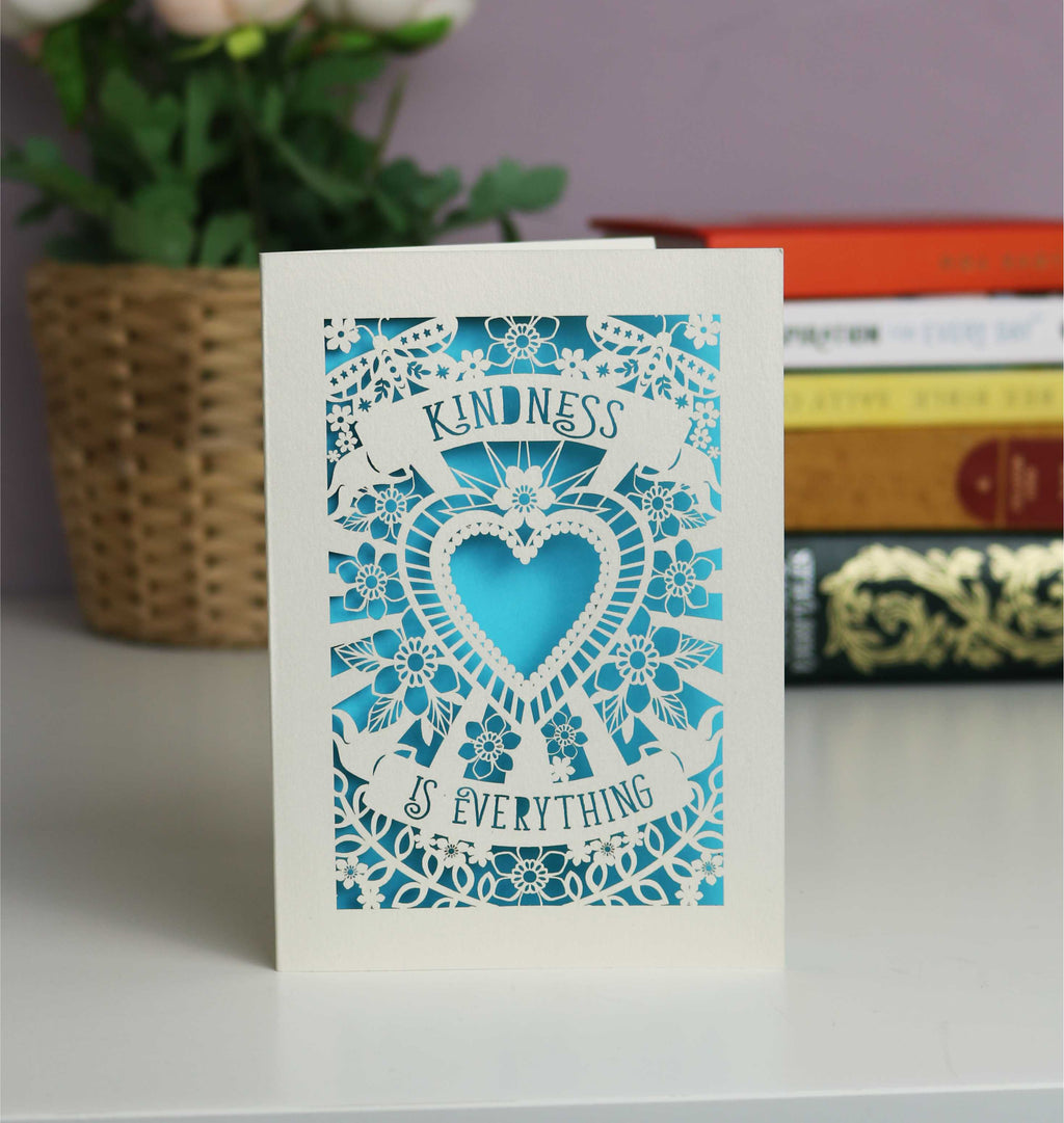 Gorgeous cream and peacock blue papercut card with Kindness is everything on two banners. A central heart with butterflies and flowers around.