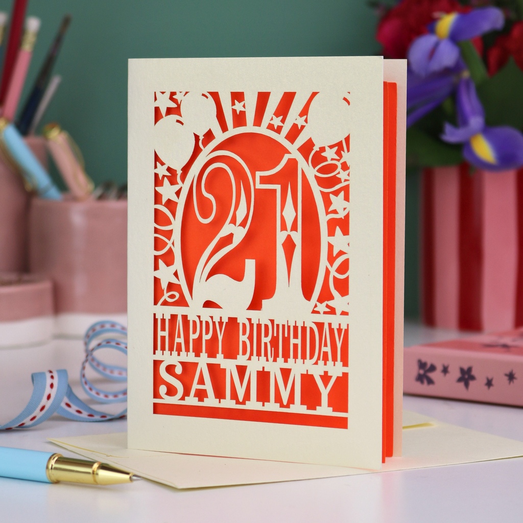 Personalized 21st birthday card with number 21 and decorative elements, and text "Happy Birthday Sammy" on a desk with stationery items.