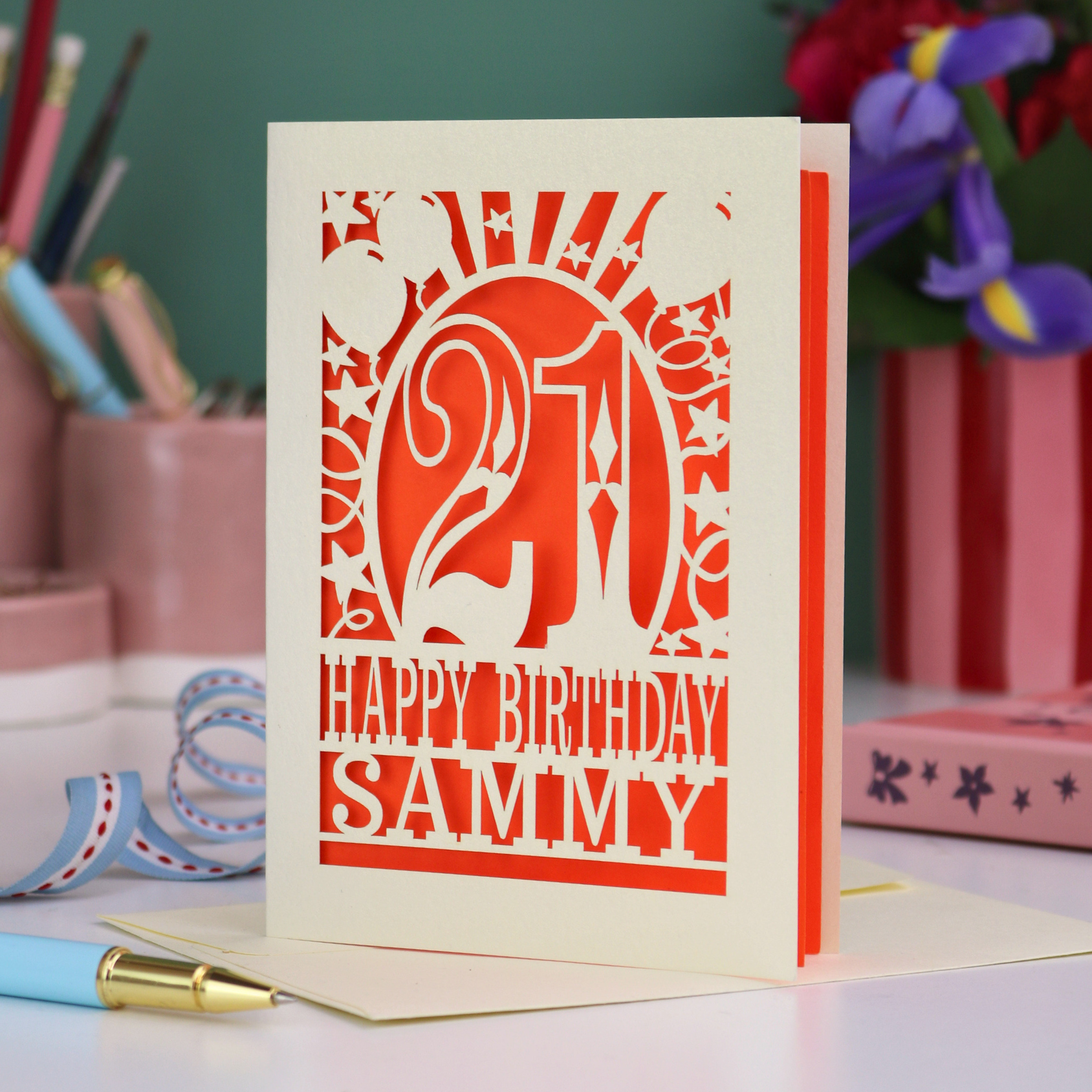 Personalized 21st birthday card with number 21 and decorative elements, and text "Happy Birthday Sammy" on a desk with stationery items.