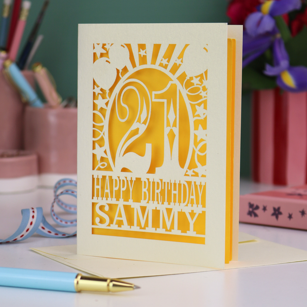 Personalized 21st birthday card with number 21 and decorative elements, and text "Happy Birthday Sammy" on a desk with stationery items.