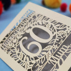 Decorative laser cut birthday card with cut-out numbers '60' and floral patterns on a blue background