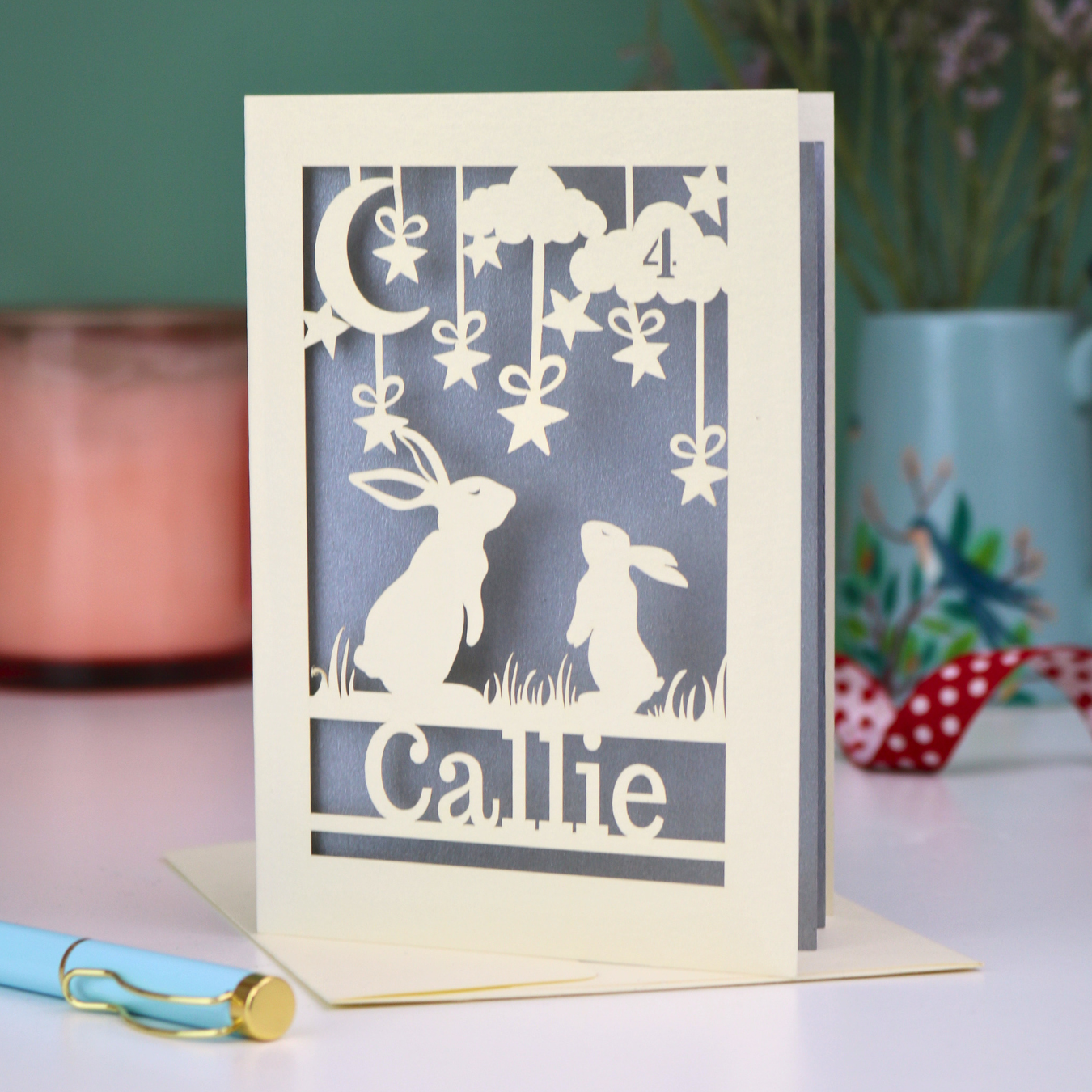 Personalised laser cut birthday card with cut-out rabbits looking up at the moon design and 'Callie' text on a silver background