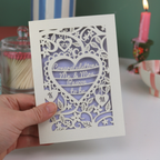 Hand holding a laser-cut engagement card with decorative patterns and text.