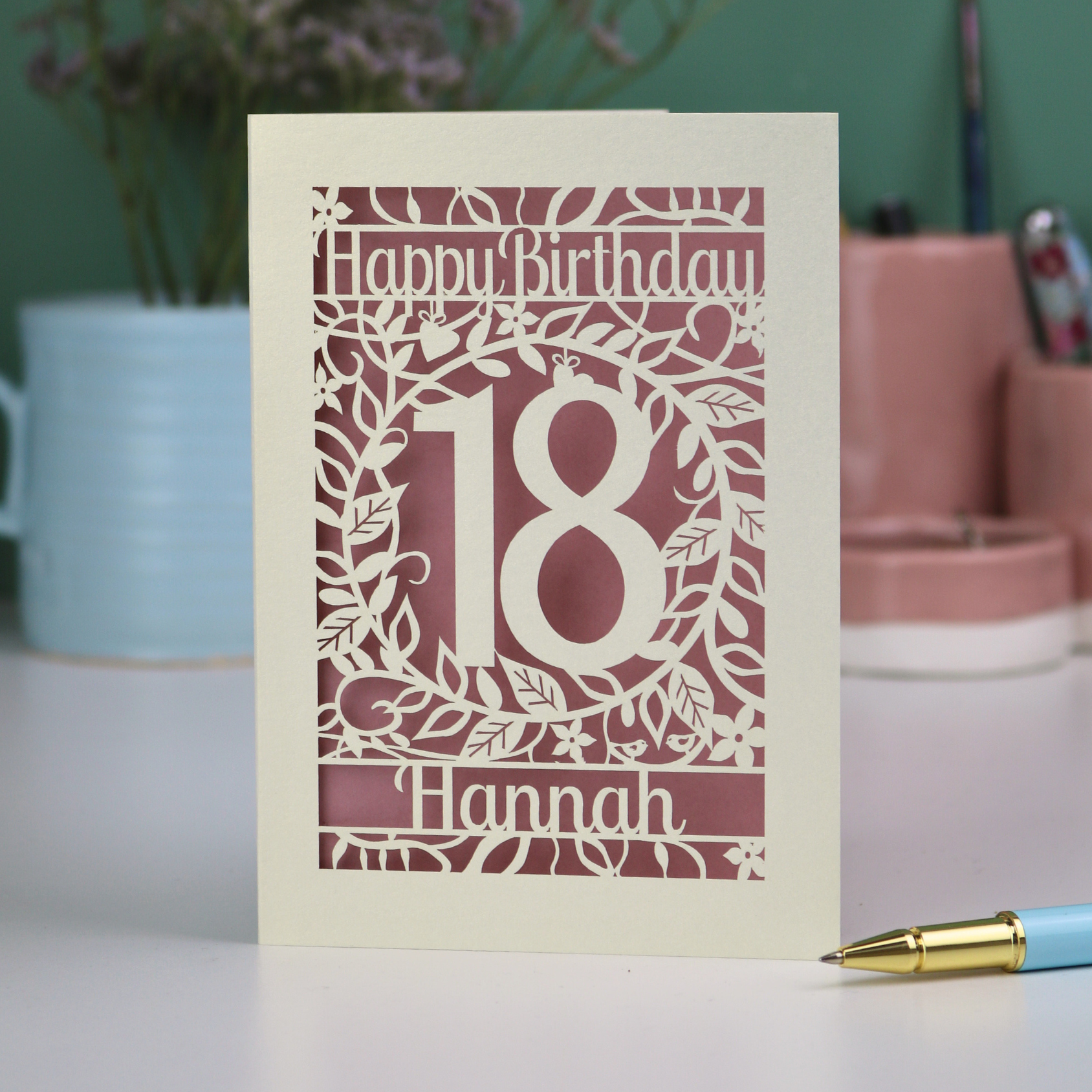 18th Birthday card with 'Happy Birthday Hannah' on a desk with a pen and plant.