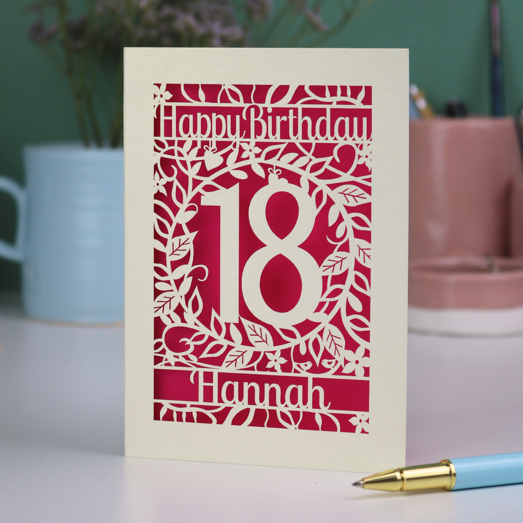 Personalised 18th Birthday card with 'Happy Birthday 18 Hannah' on a desk with a pen and mug.