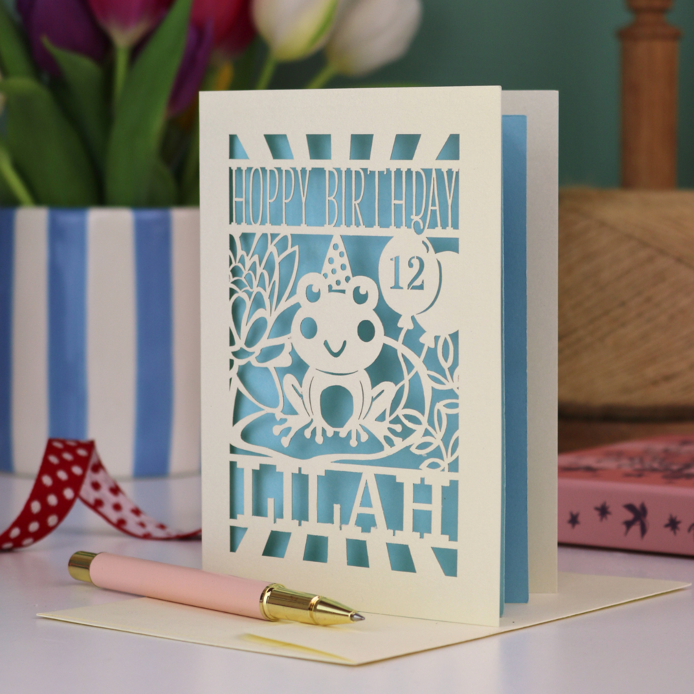 A personalised birthday card for kids, personalised with a name and age, featuring a laser cut frog design and the text "Hoppy Birthday"