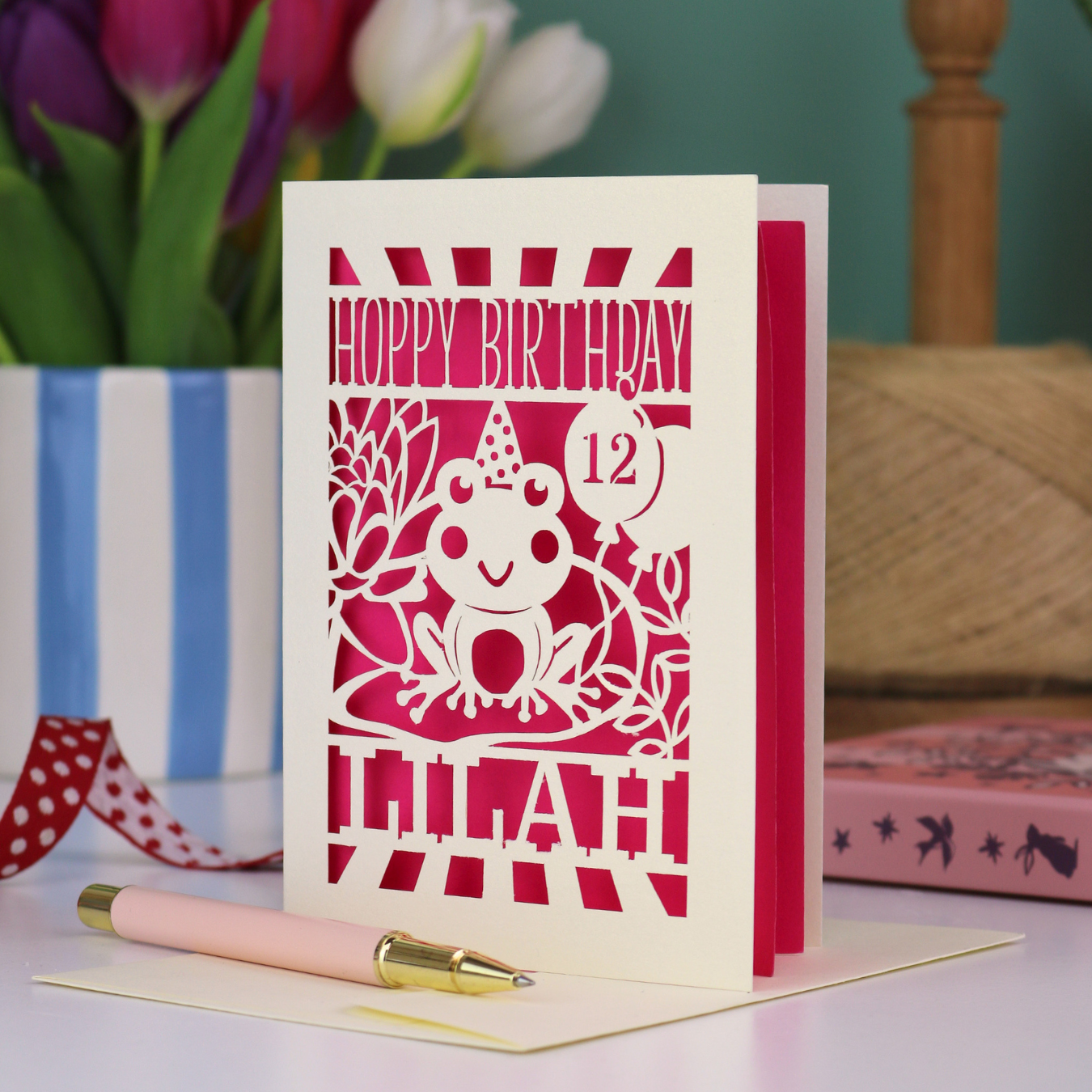 A kids' birthday card, personalised with a name and age, featuring a laser cut frog design and the text "Hoppy Birthday"
