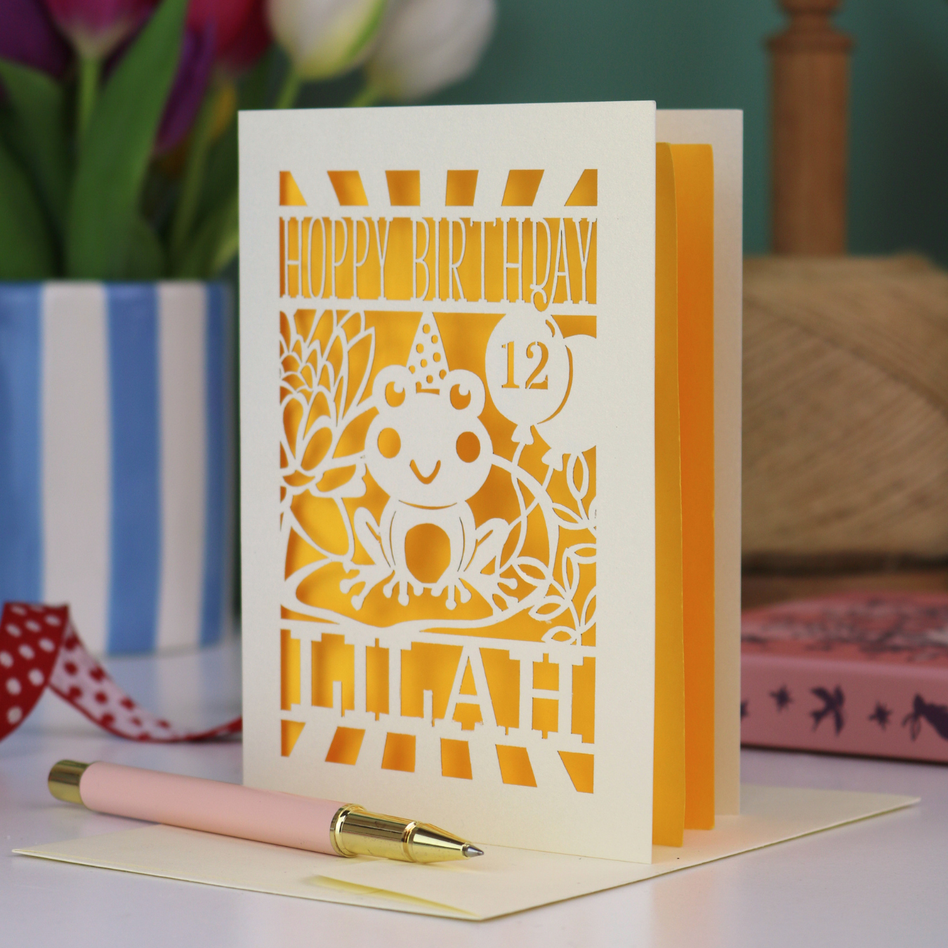 A keepsake frog birthday card, personalised with a name and age, featuring a laser cut frog design and the text "Hoppy Birthday"
