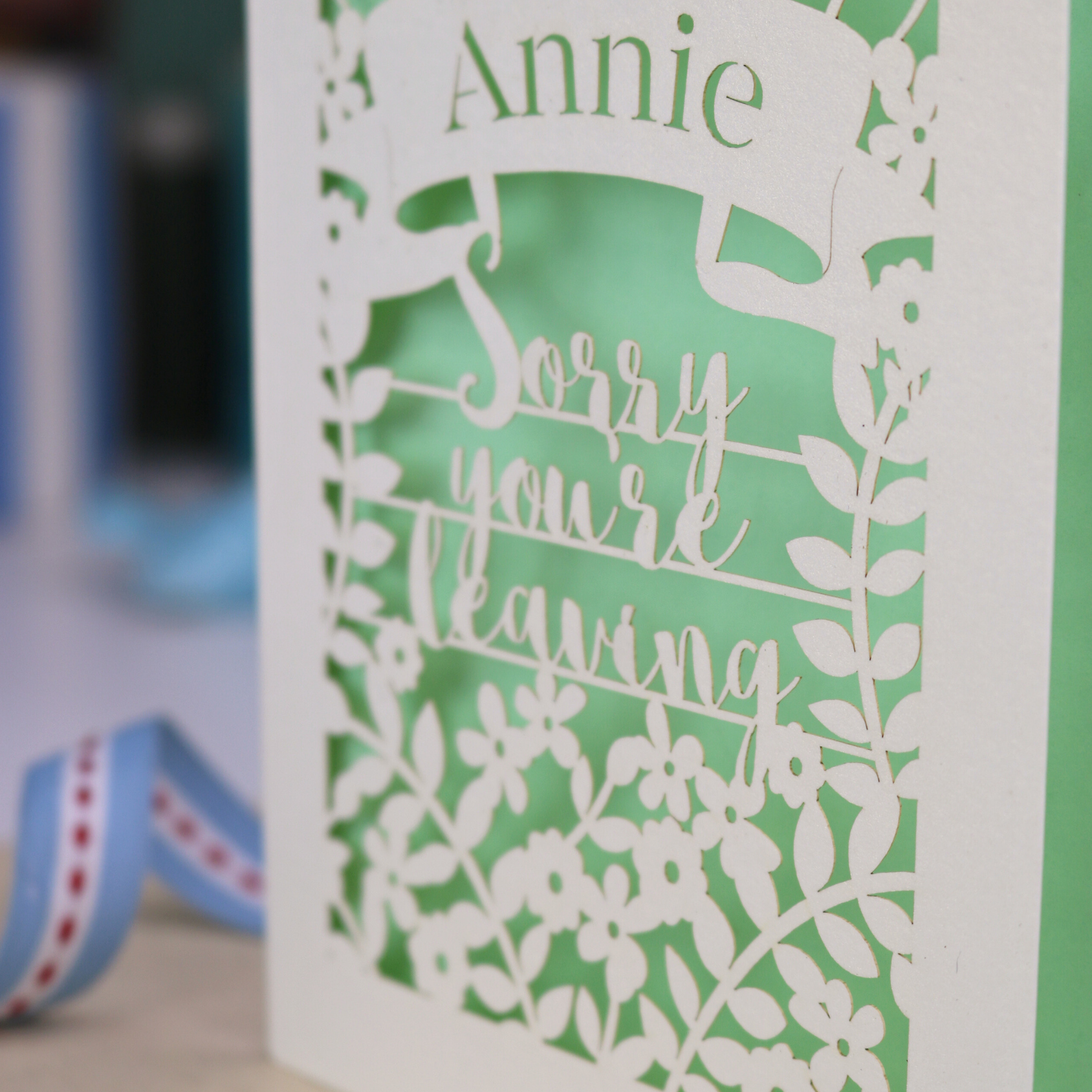 Laser cut leaving Card with 'Sorry you're leaving' message on a desk with decorative items.