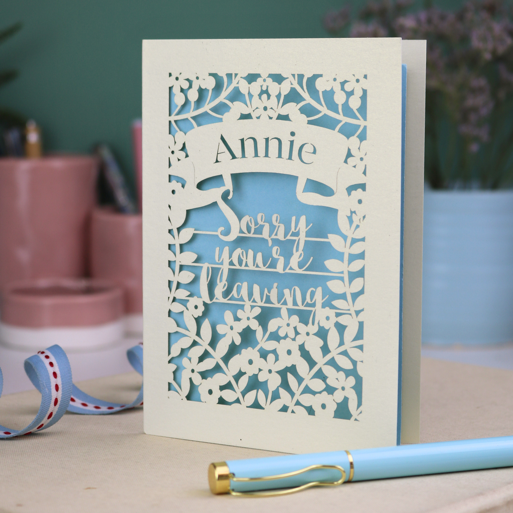 Laser cut goodbye Card with 'Sorry you're leaving' message on a desk with decorative items.