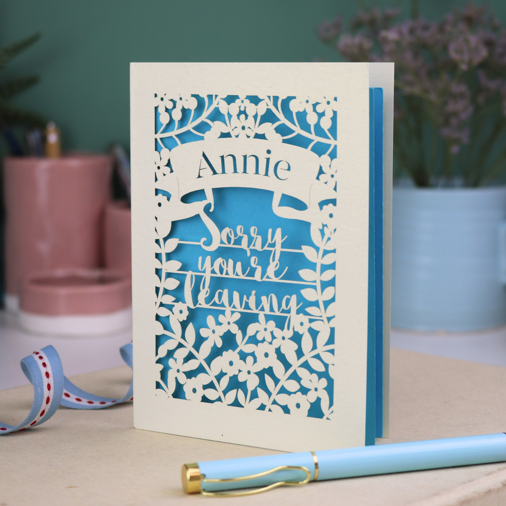 Laser cut leaving Card with 'Sorry you're leaving' message on a desk with decorative items.