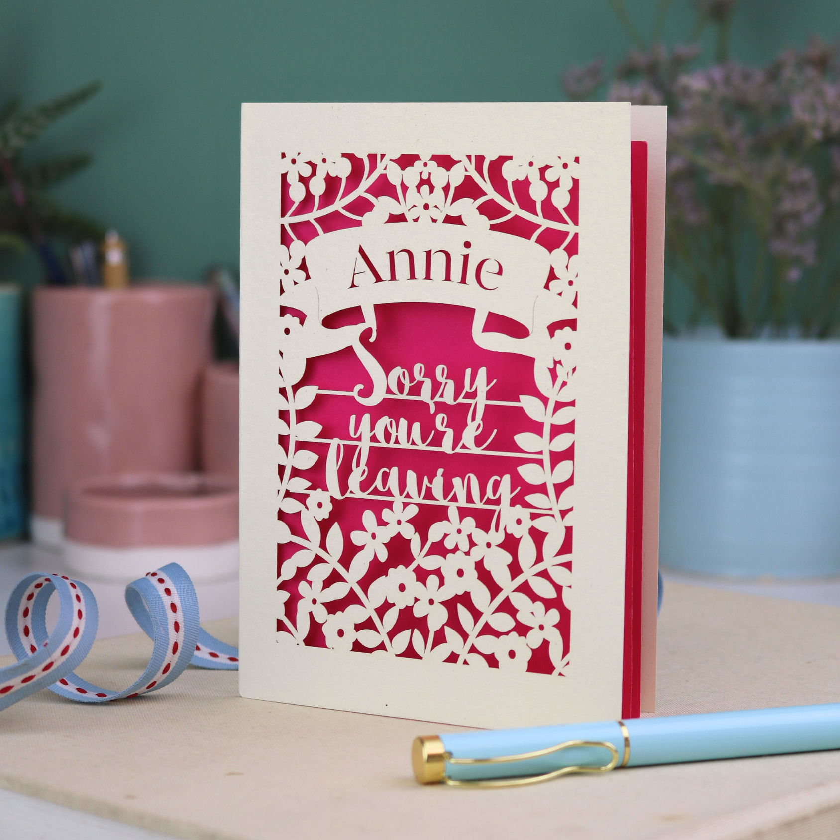 Laser cut leaving Card with 'Sorry you're leaving' message on a desk with decorative items.