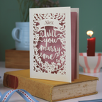 Proposal card with 'Will you marry me?' on a book with a blurred background