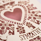 A close up of a cream laser cut sympathy card with cut out heart and flowers design 