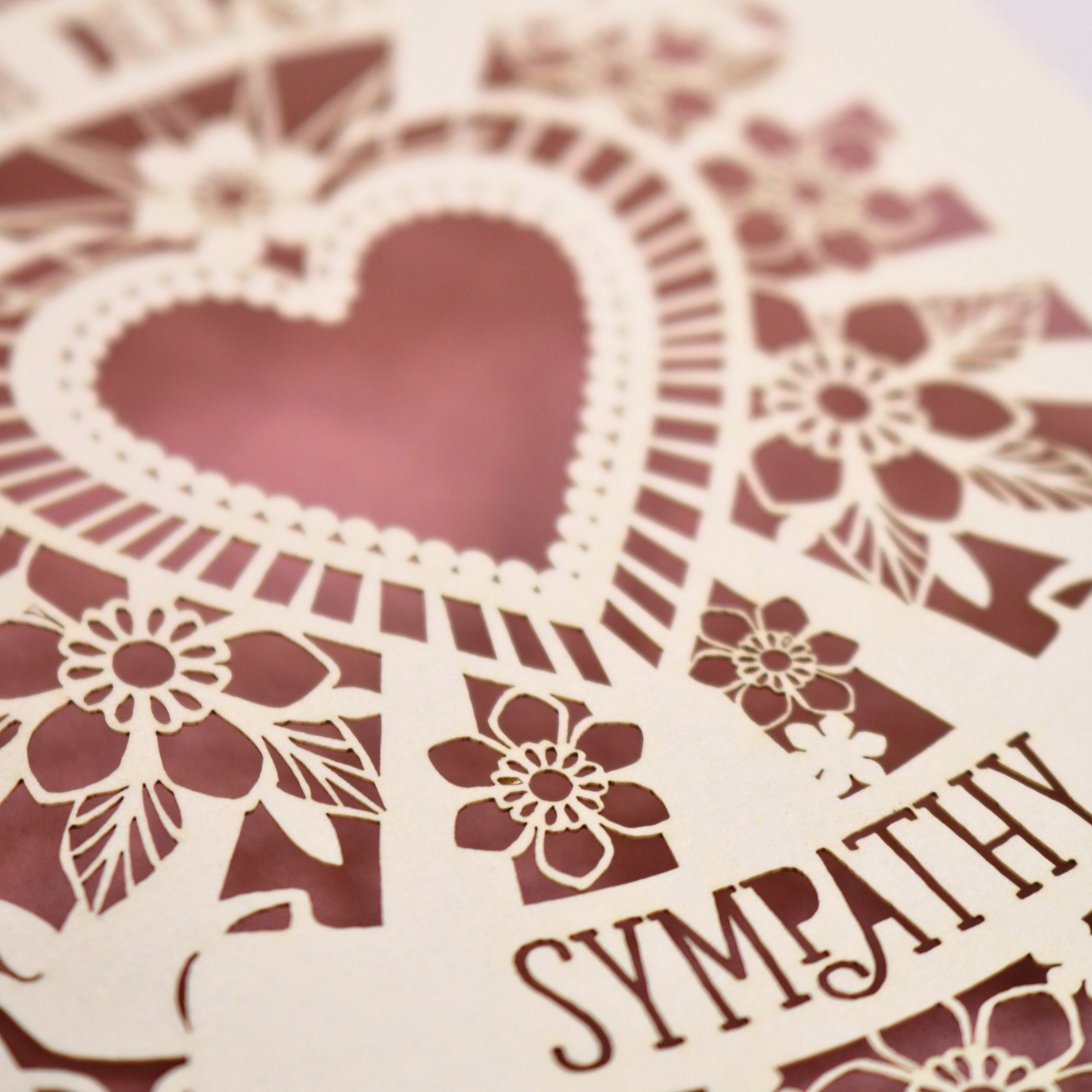 A close up of a cream laser cut sympathy card with cut out heart and flowers design 
